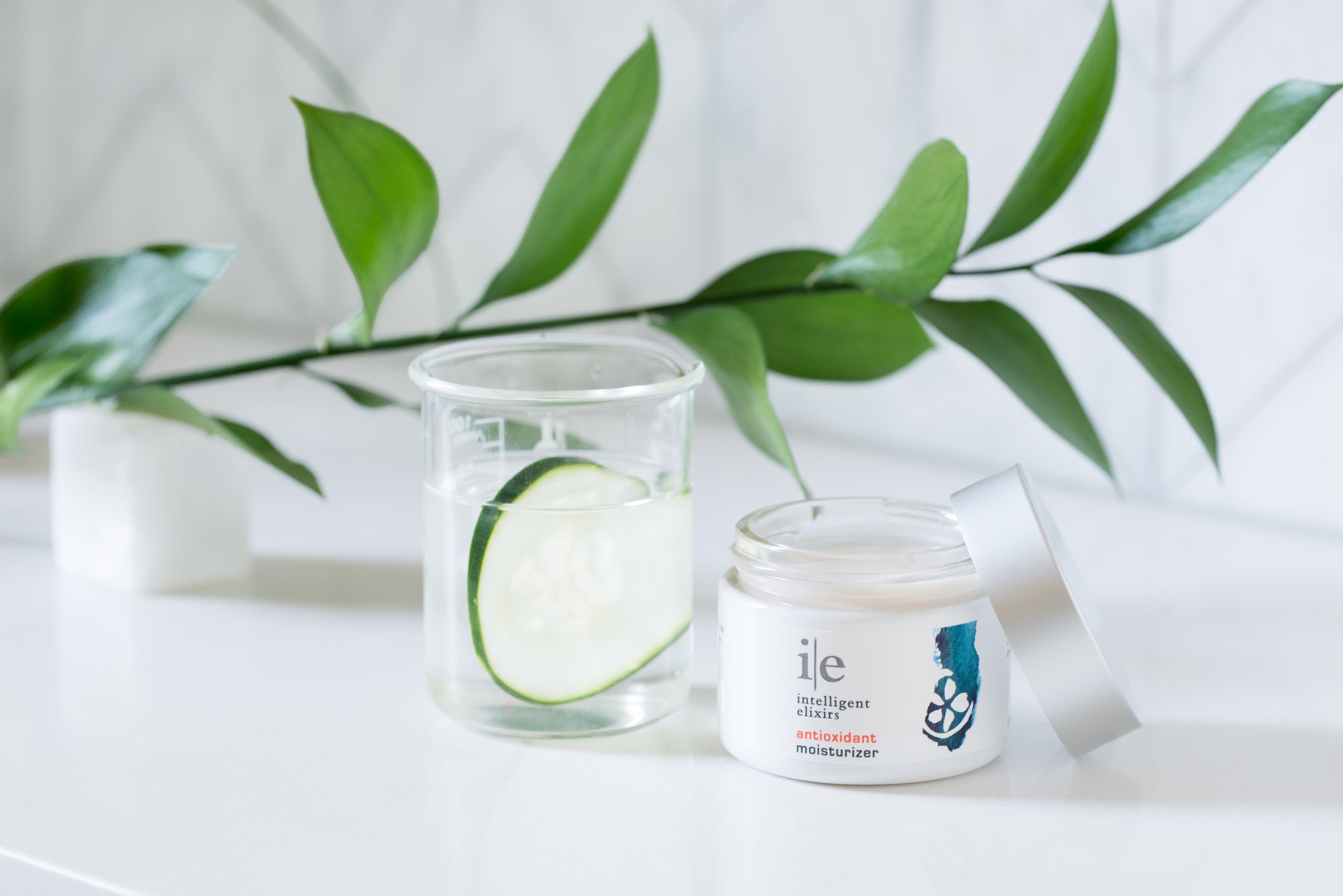 Antioxidant Facial Moisturizer on a counter next to a cucumber in water
