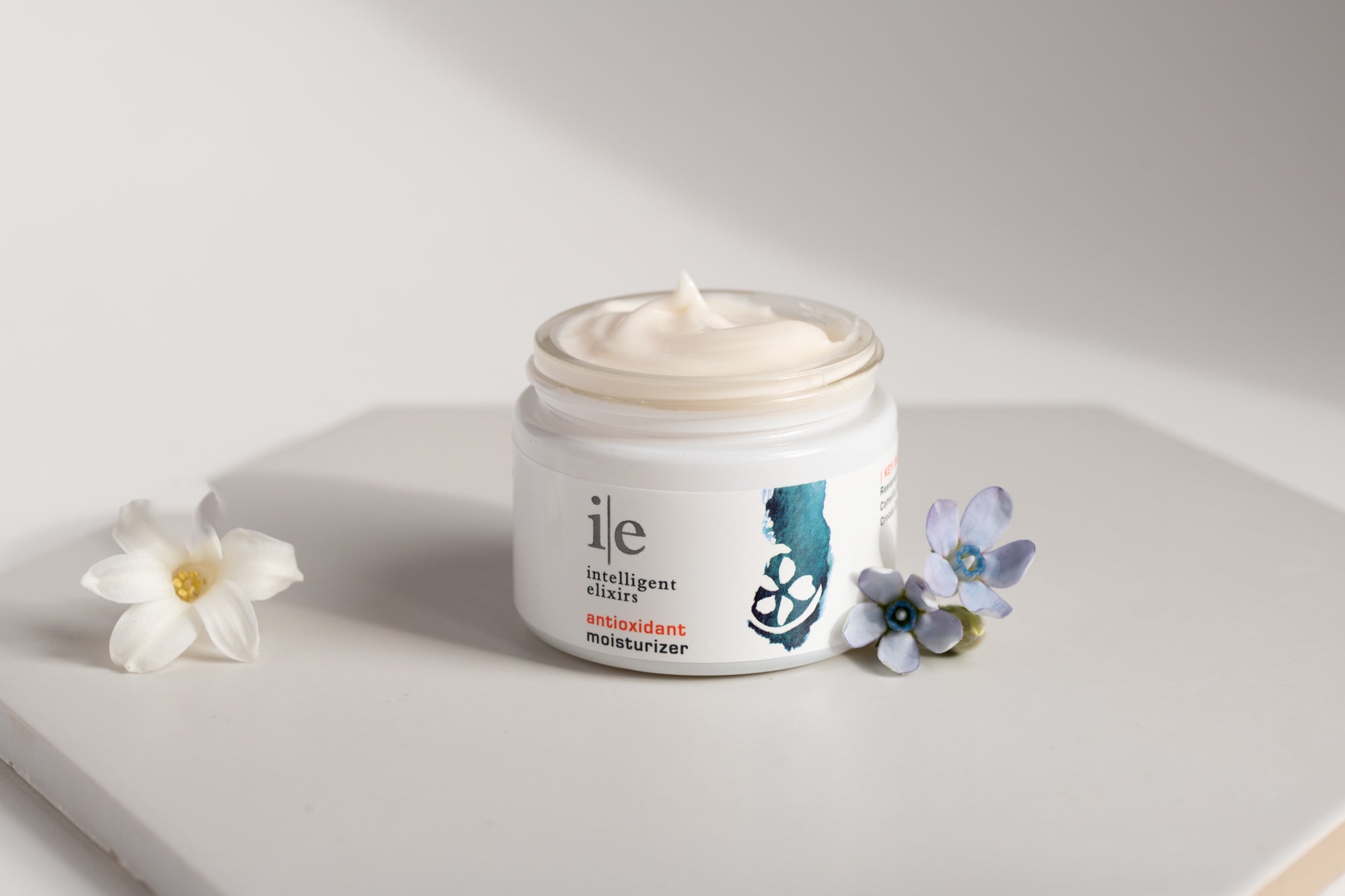 Antioxidiant Facial Moisturizer showing texture of cream next to flower petals