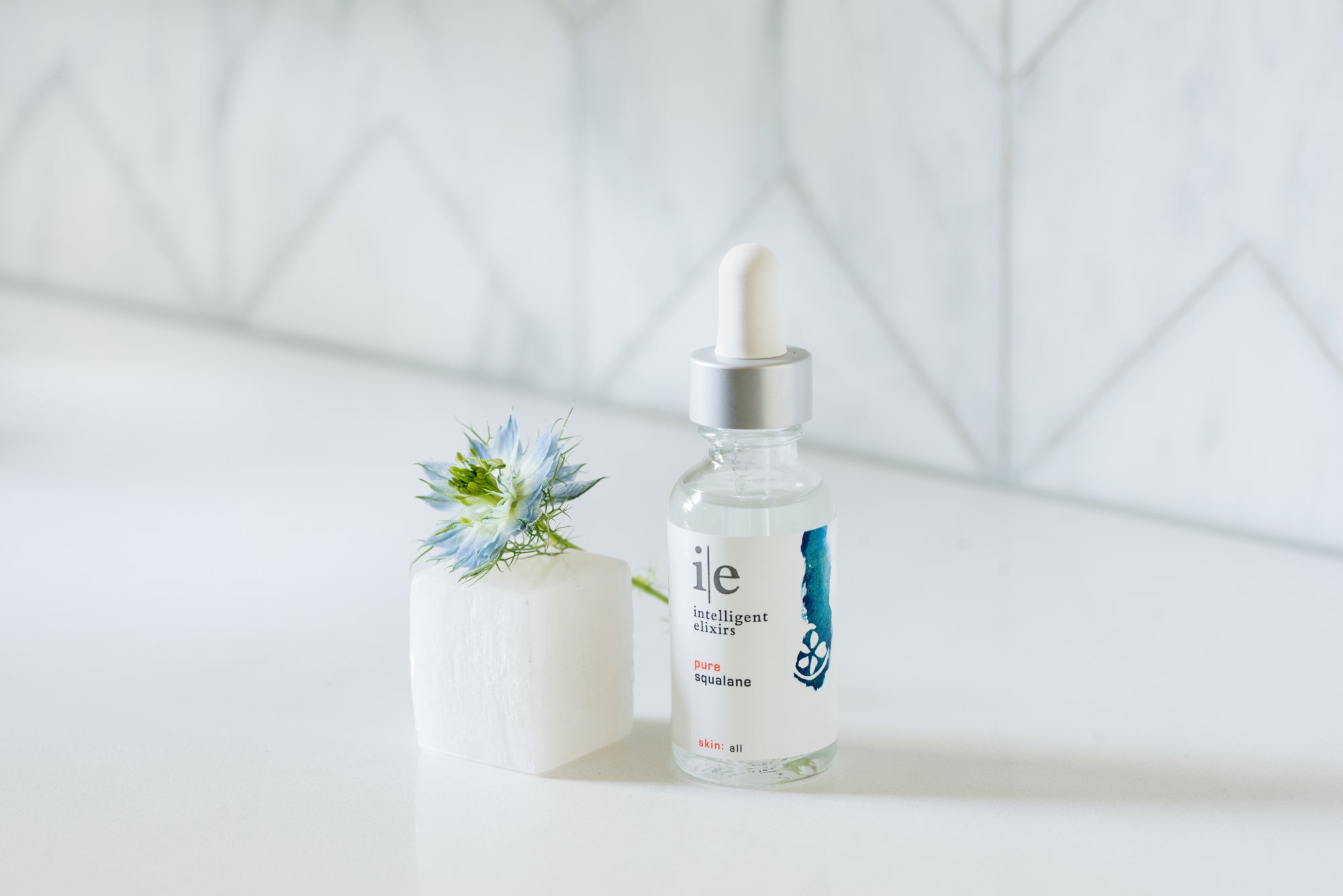 Pure Squalane Facial Serum next to flower petals on a clear cube