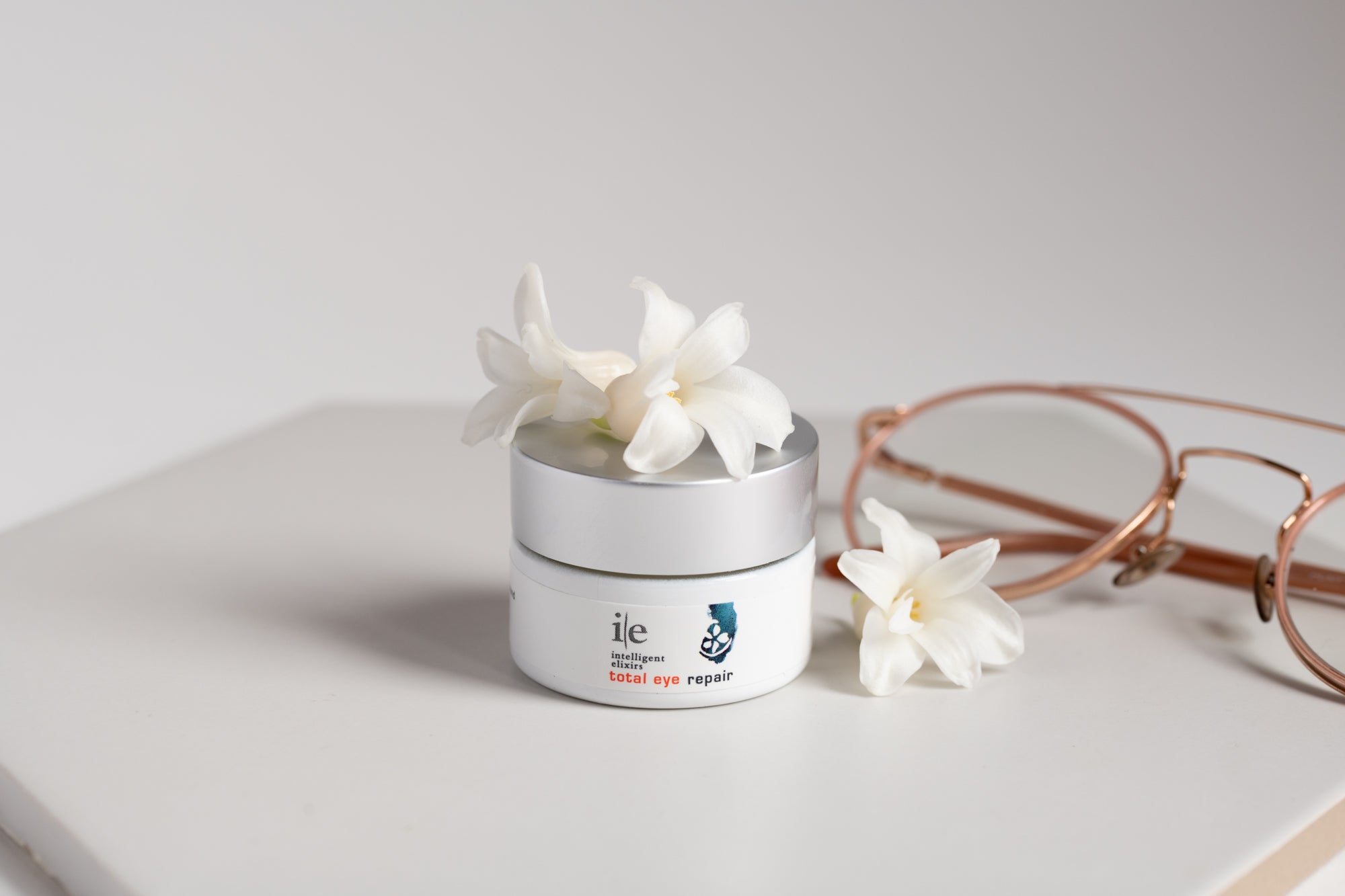 Total Eye Repair Eye Cream jar on a counter with flower petals and a pair of glasses